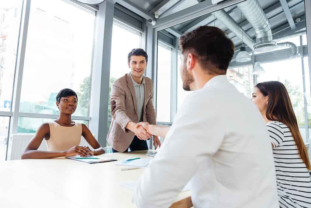 Smiling young people shaking hands on business meeting in office